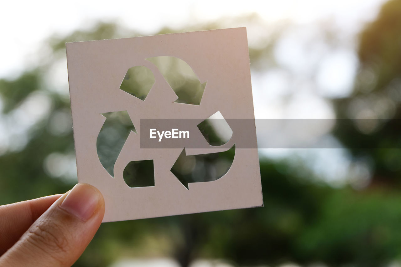 Close-up of hand holding recycling symbol against trees