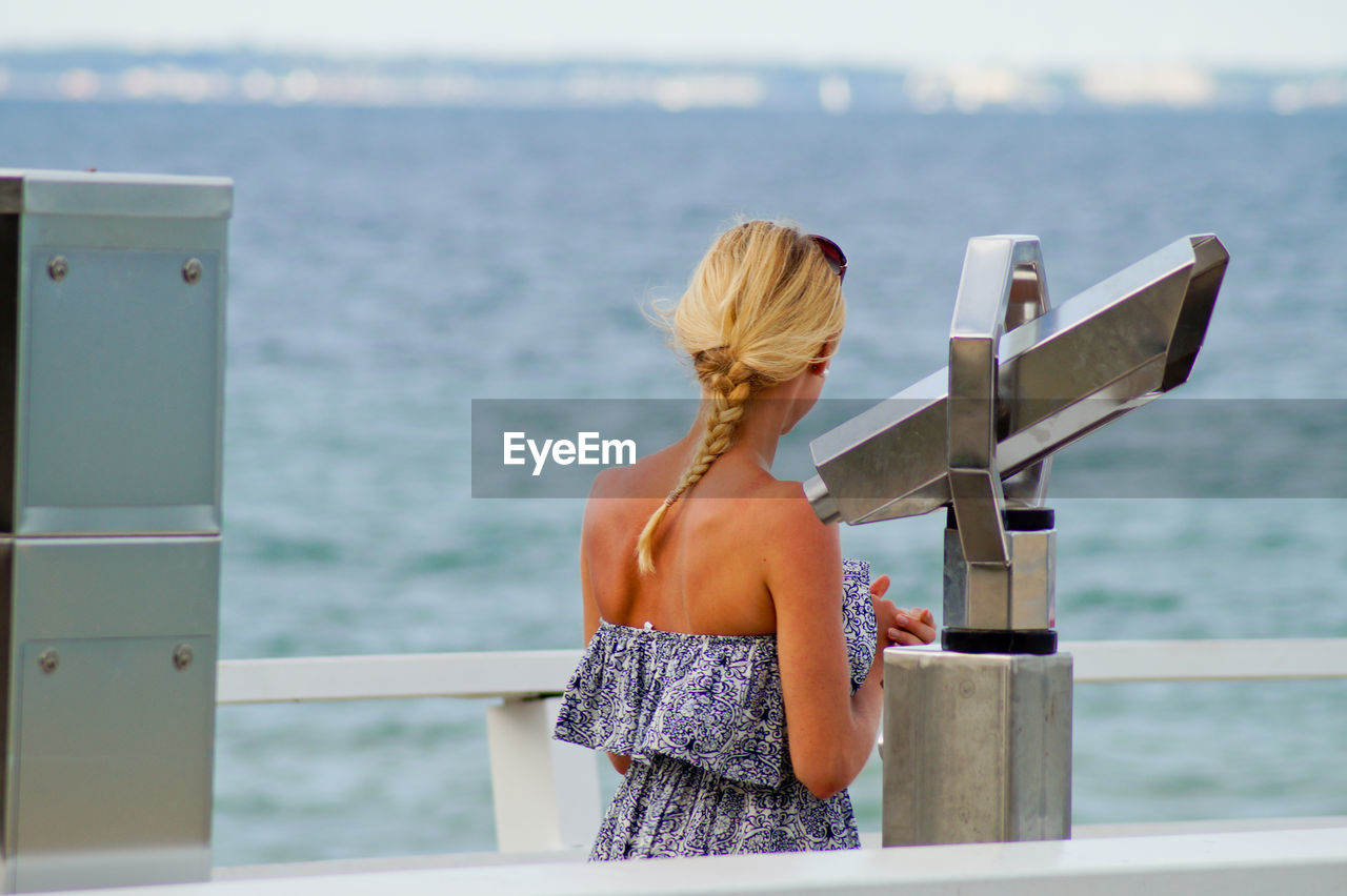 Rear view of woman standing by binoculars at observation point