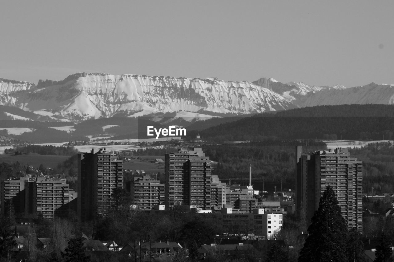 High angle view of buildings in city by snowcapped mountain against clear sky