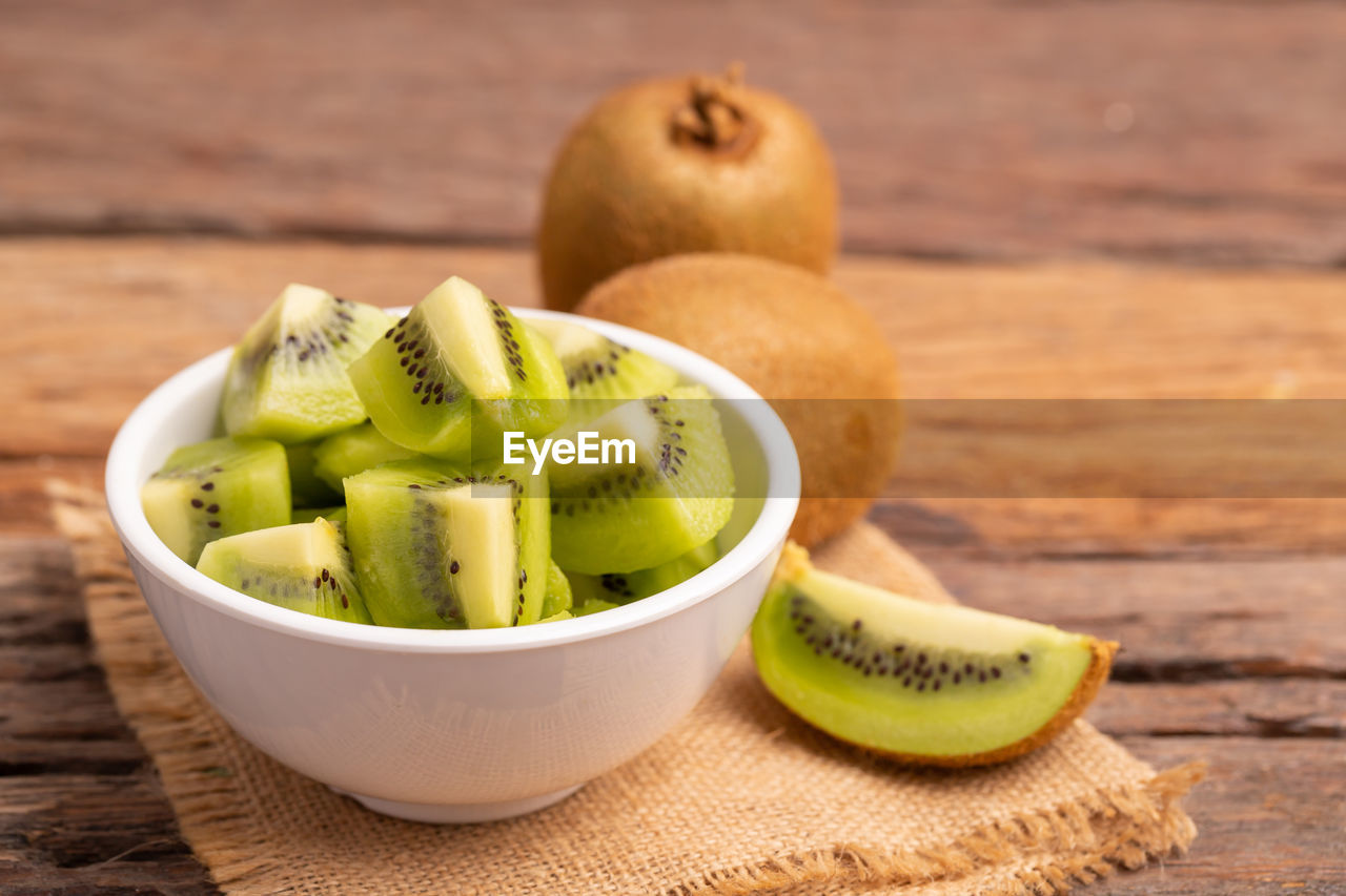 Slices of fresh kiwi in a white bowl placed on the old wooden table