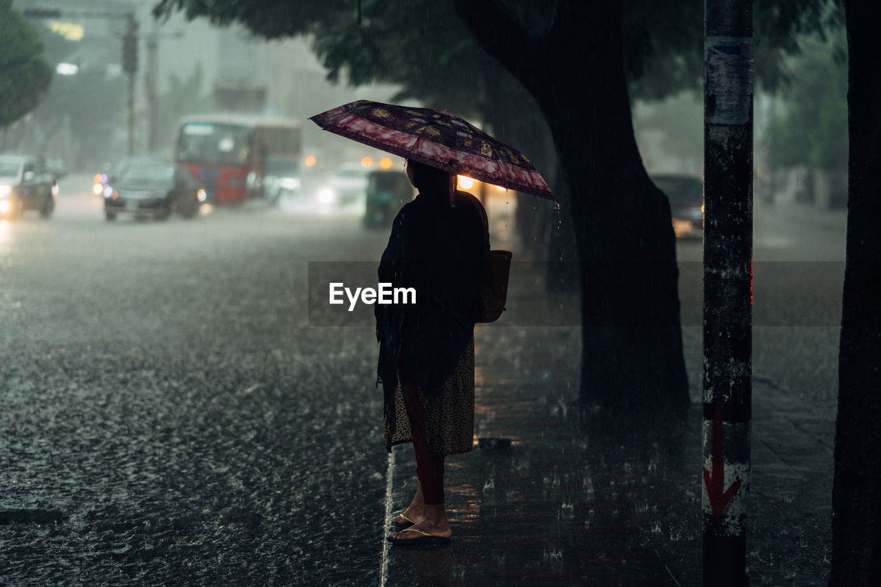 Rear view of person walking on wet street during rainy season