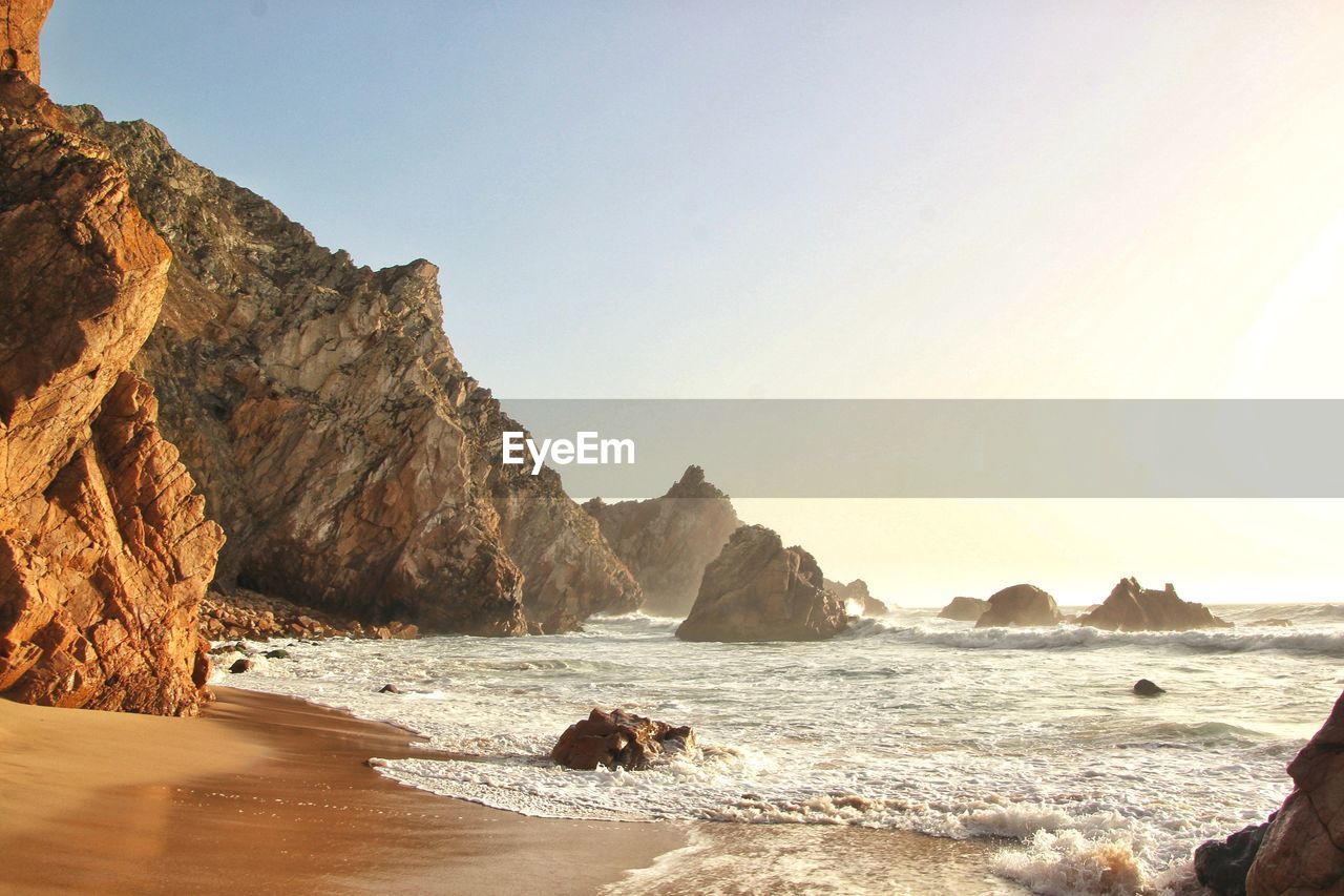 Rock formation on beach against clear sky during sunset 