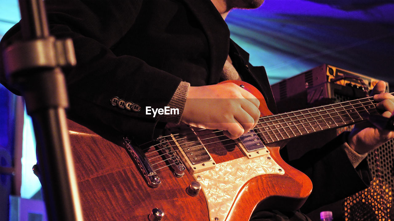 Midsection of man playing electric guitar during music concert