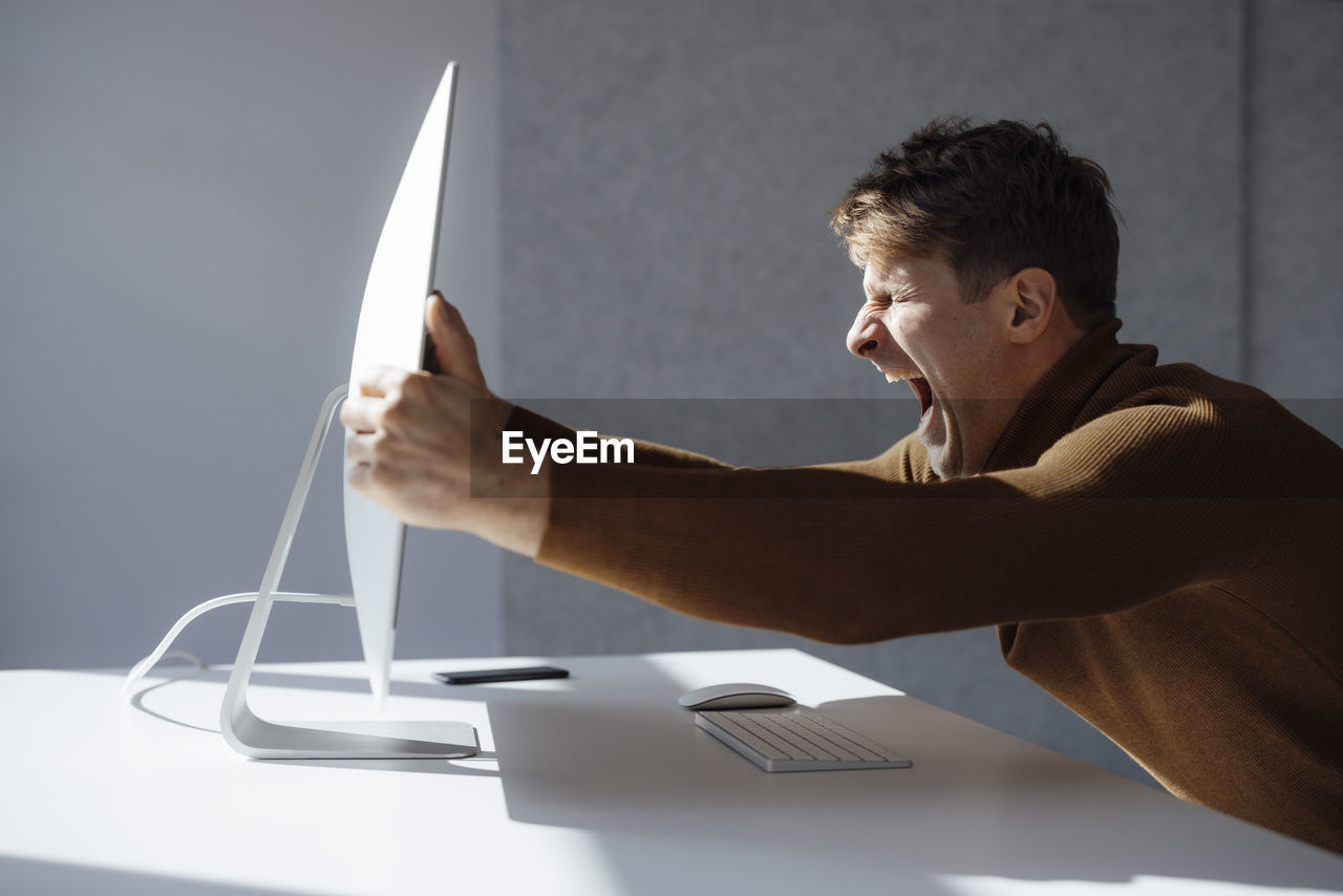 Businessman holding computer monitor screaming at desk in office