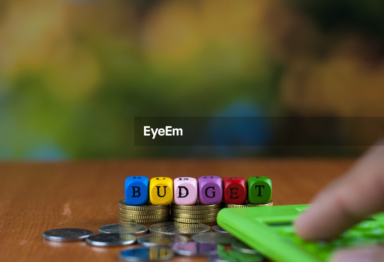 Close-up of hand using calculator by text made with toy blocks over coins on table