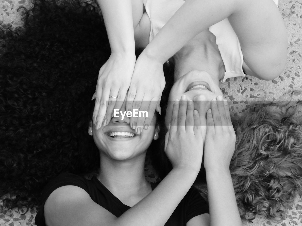 High angle view of smiling mother and daughter covering eyes while lying on floor