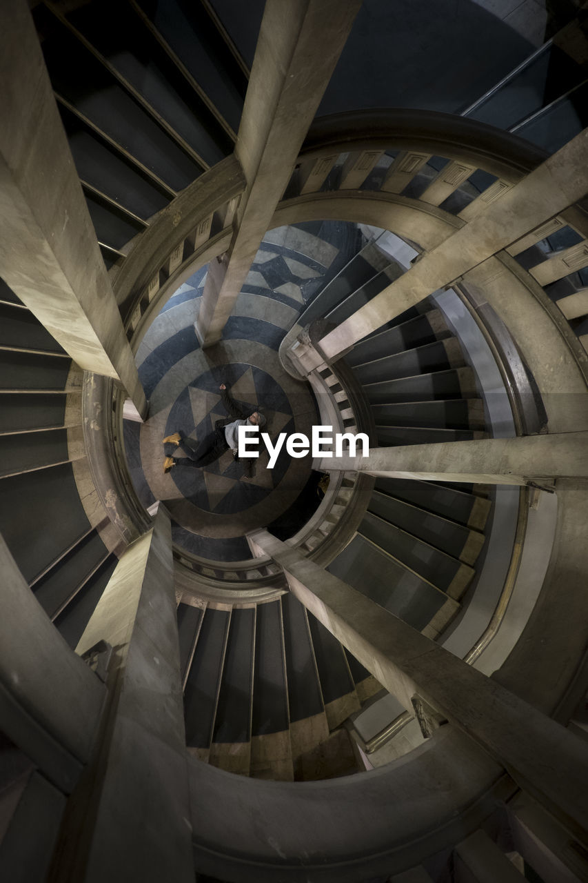 Directly above view of woman lying by spiral staircase in building