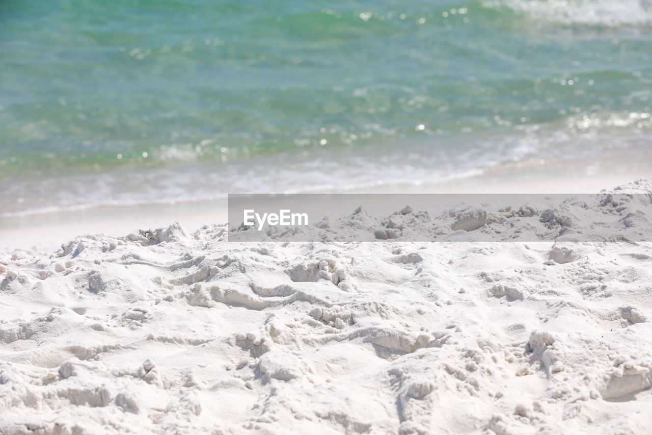 Close up shot of the white sandy beach in florida with the green ocean water in the background.