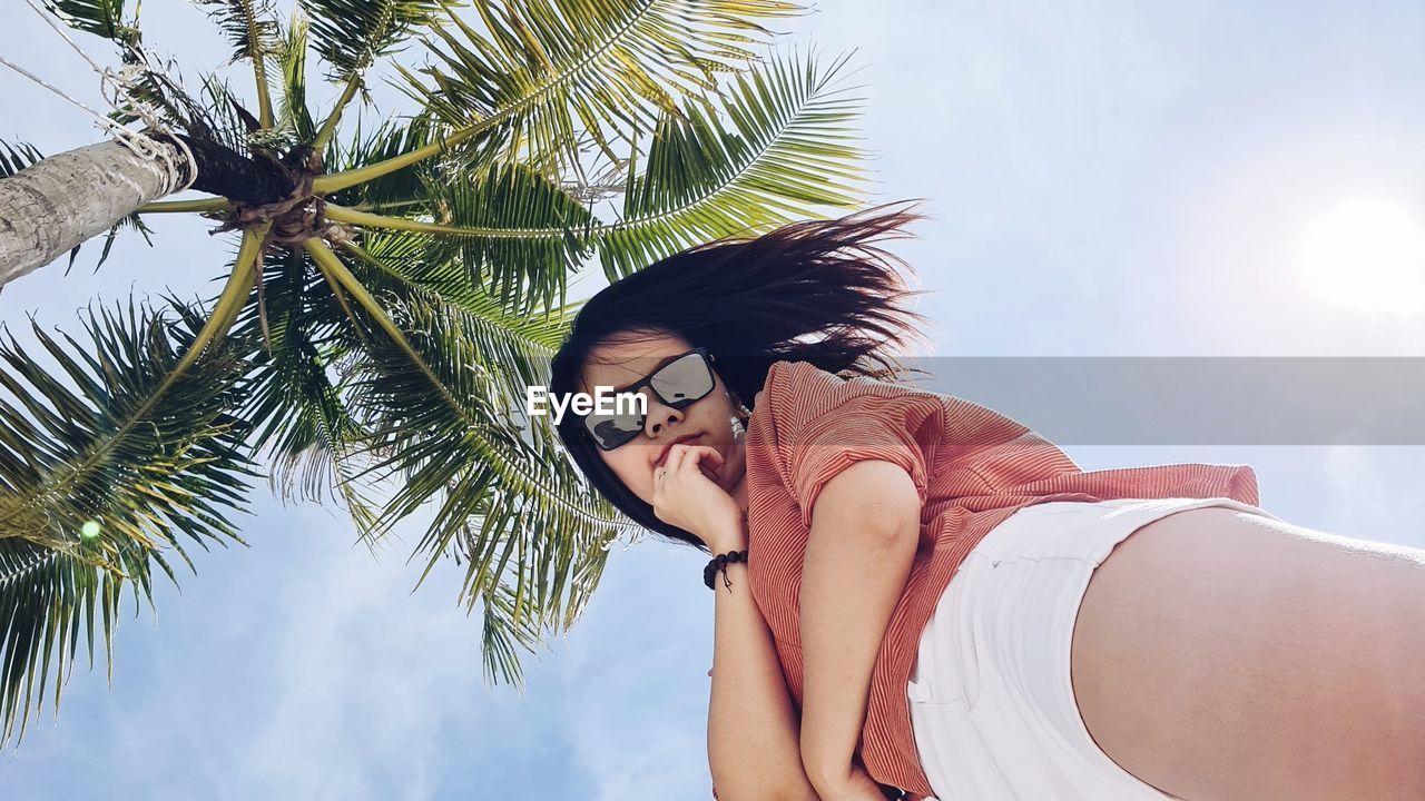 Low angle view of young woman on palm tree against sky