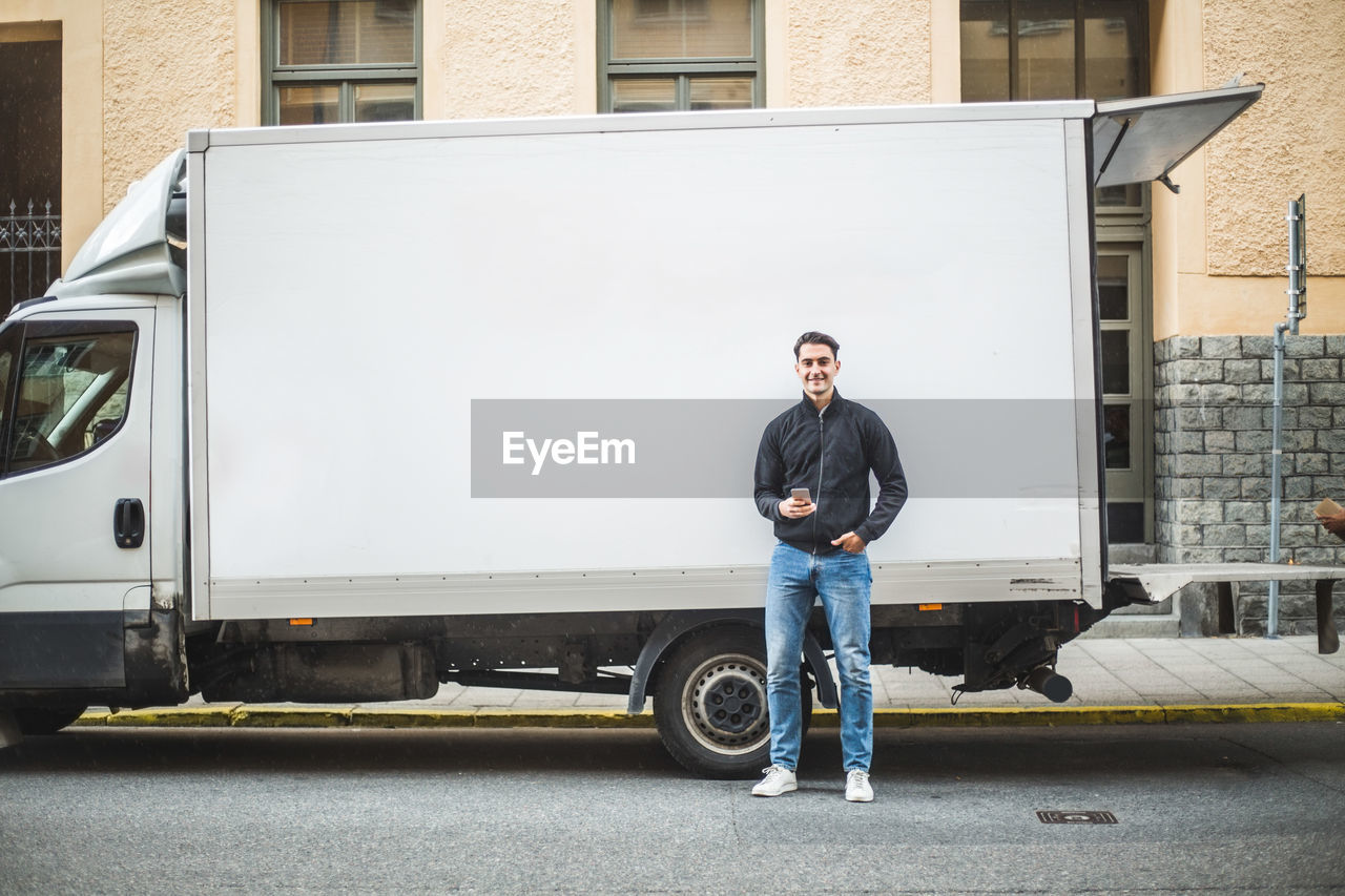 Portrait of male mover standing against truck on street in city
