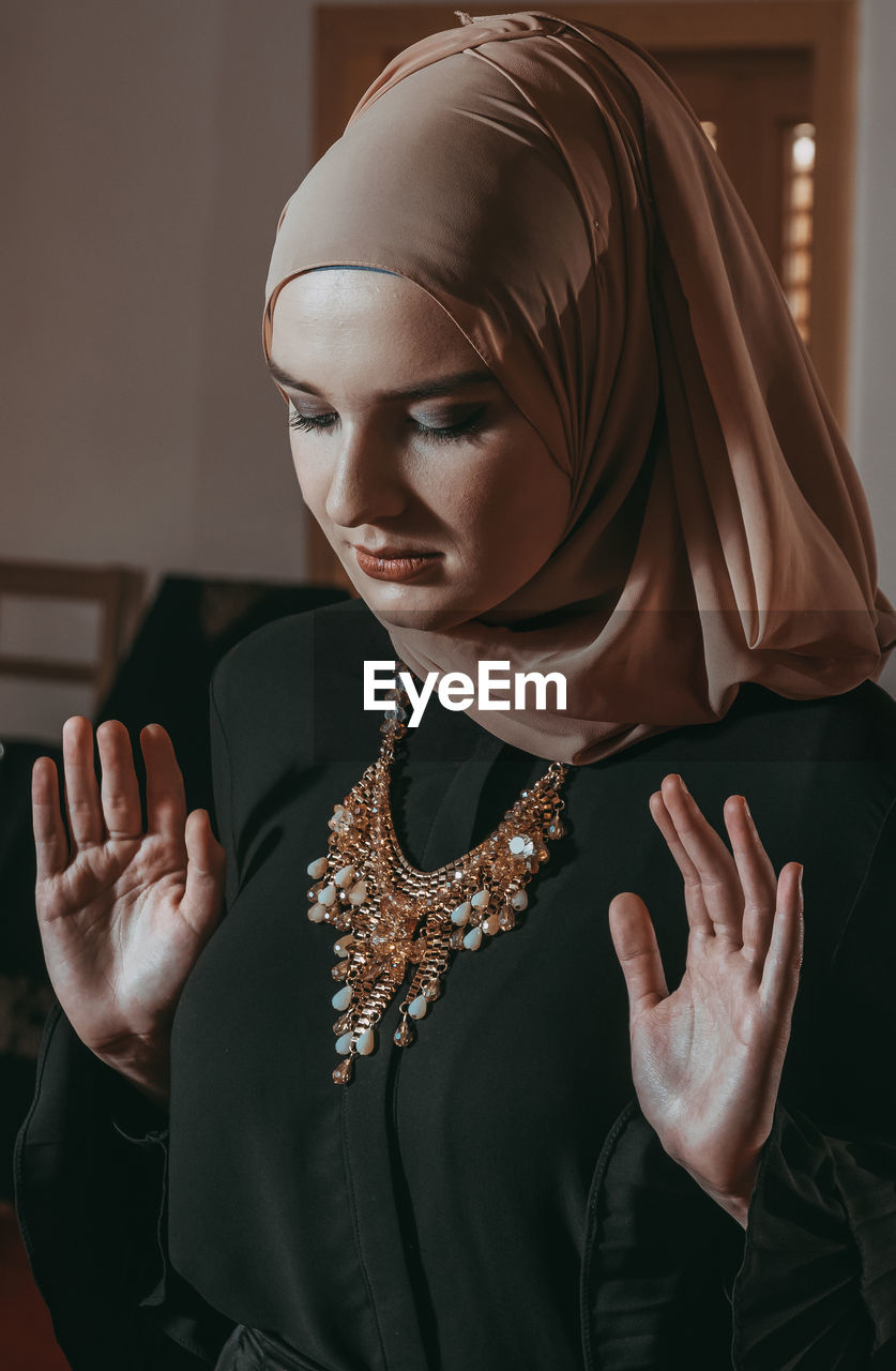 Close-up of young woman wearing hijab praying indoors