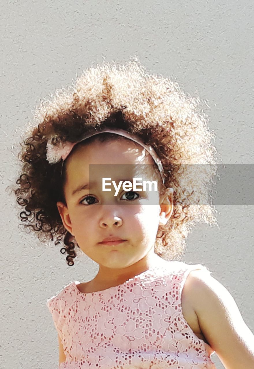 Portrait of cute girl with curly hair against wall