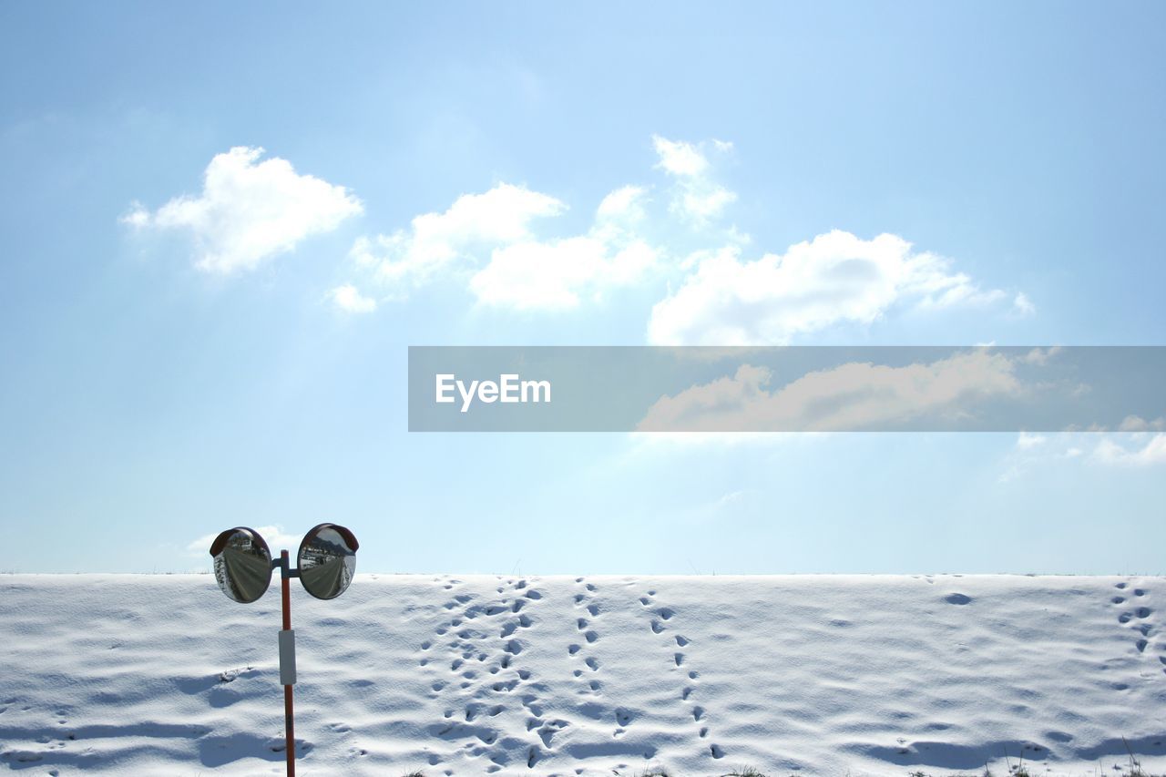 Traffic mirror on snow covered field against sky