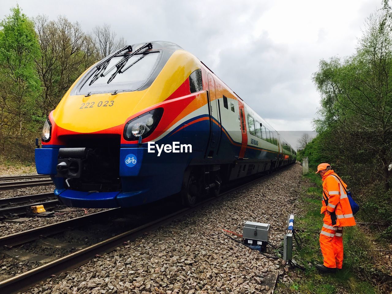 Worker standing while train moving against cloudy sky