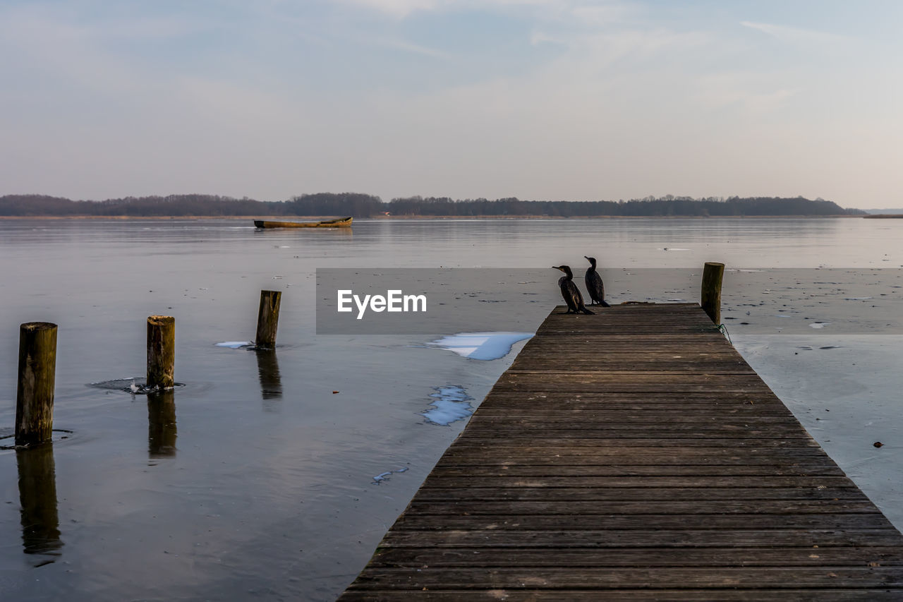 WOODEN POSTS ON PIER AT LAKE AGAINST SKY