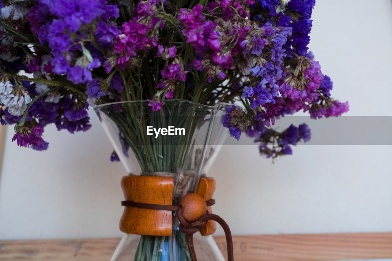 CLOSE-UP OF PURPLE FLOWERS IN VASE AGAINST WALL