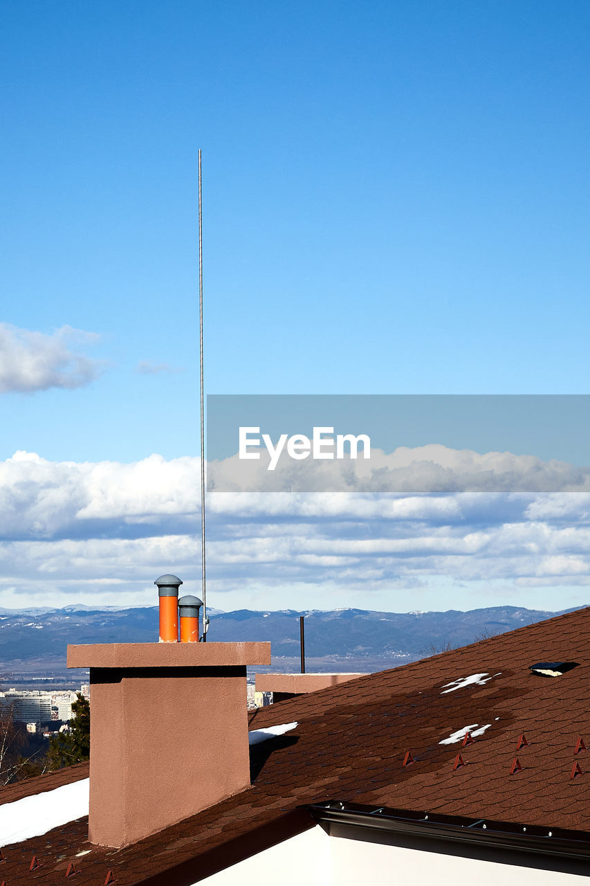 A chimney with a lightning rod against blue sky with mountains in the background