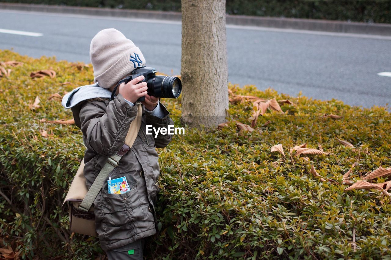 Girl photographing by hedge