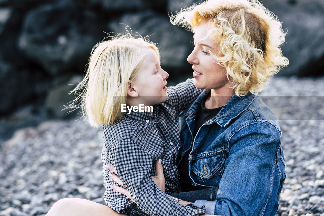 Happy woman and son with blond hair sitting at beach