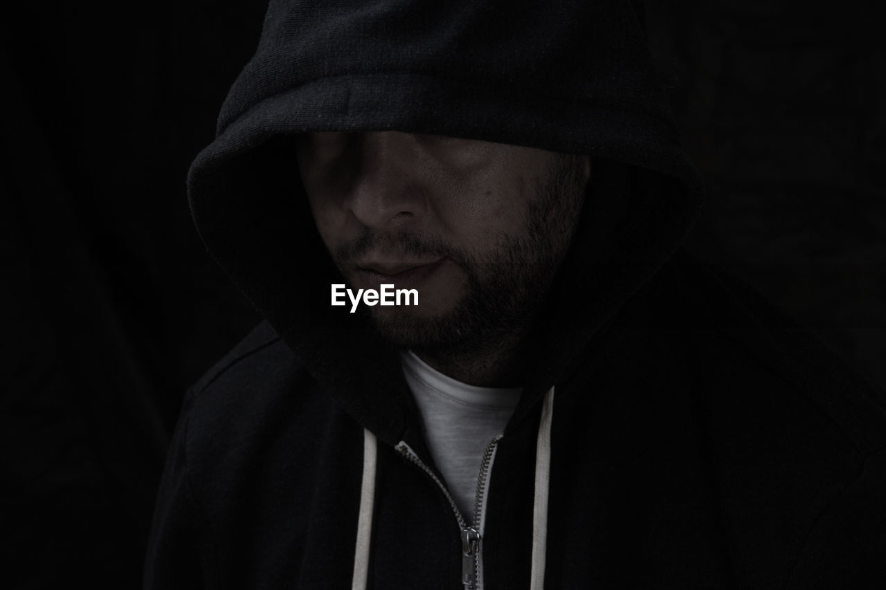 Close-up of man in hood against black background