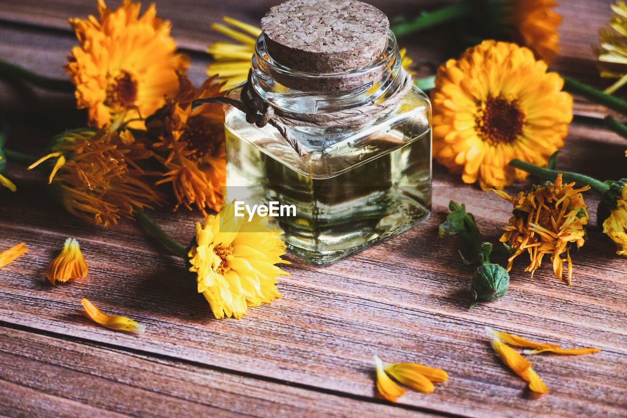 Calendula oil in glass bottle, calendula officinalis , marigold flowers on wooden table