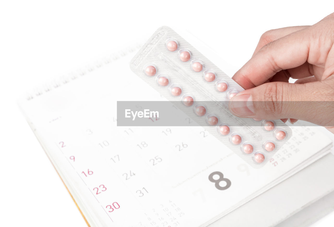Cropped image of hand holding pills with calender on white background