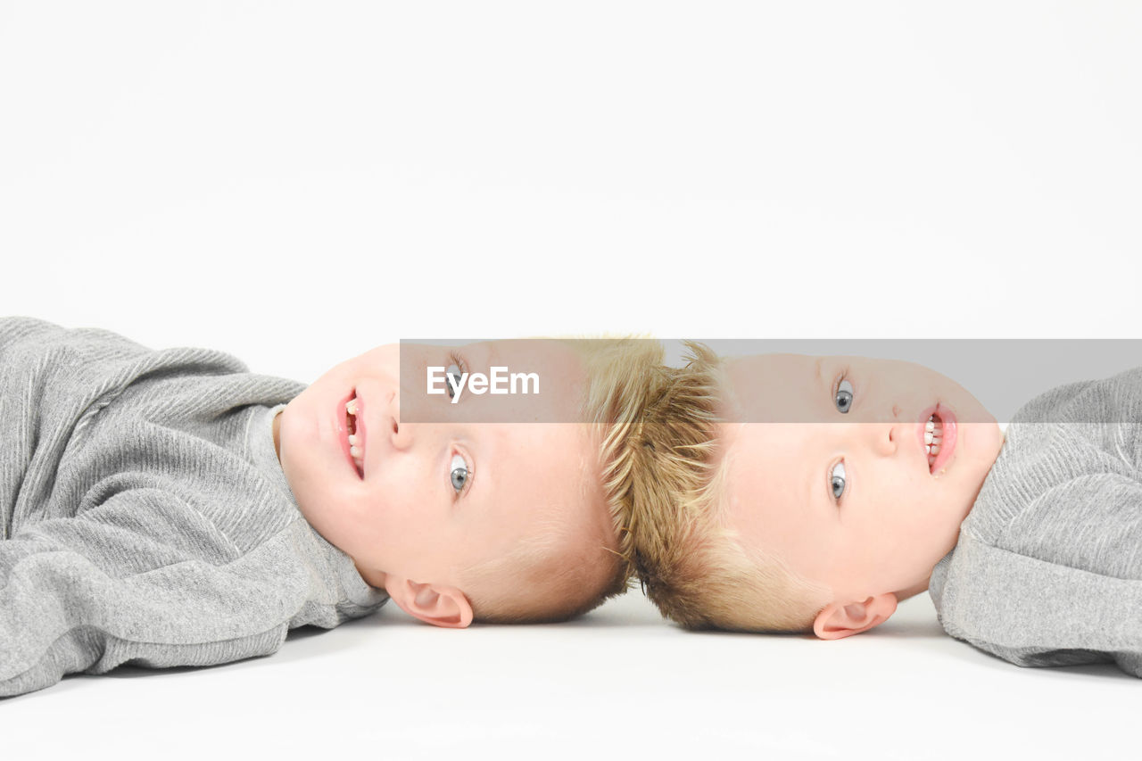 Close-up portrait of twin brothers lying against white background