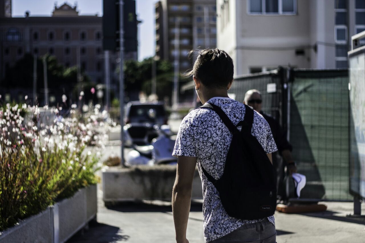 Rear view of man with backpack walking by buildings in city