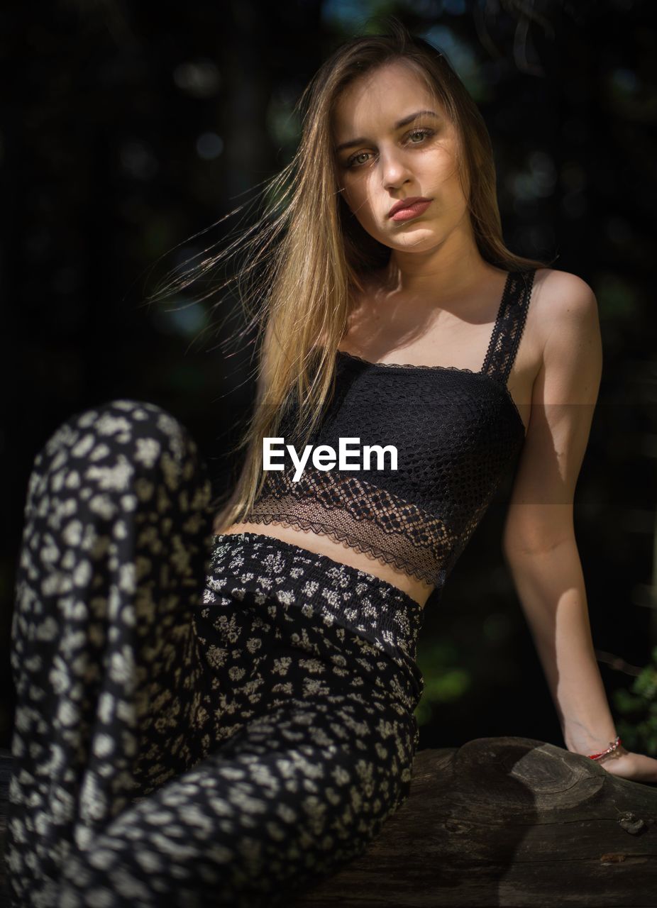 Portrait of young fashionable woman sitting on rock in forest