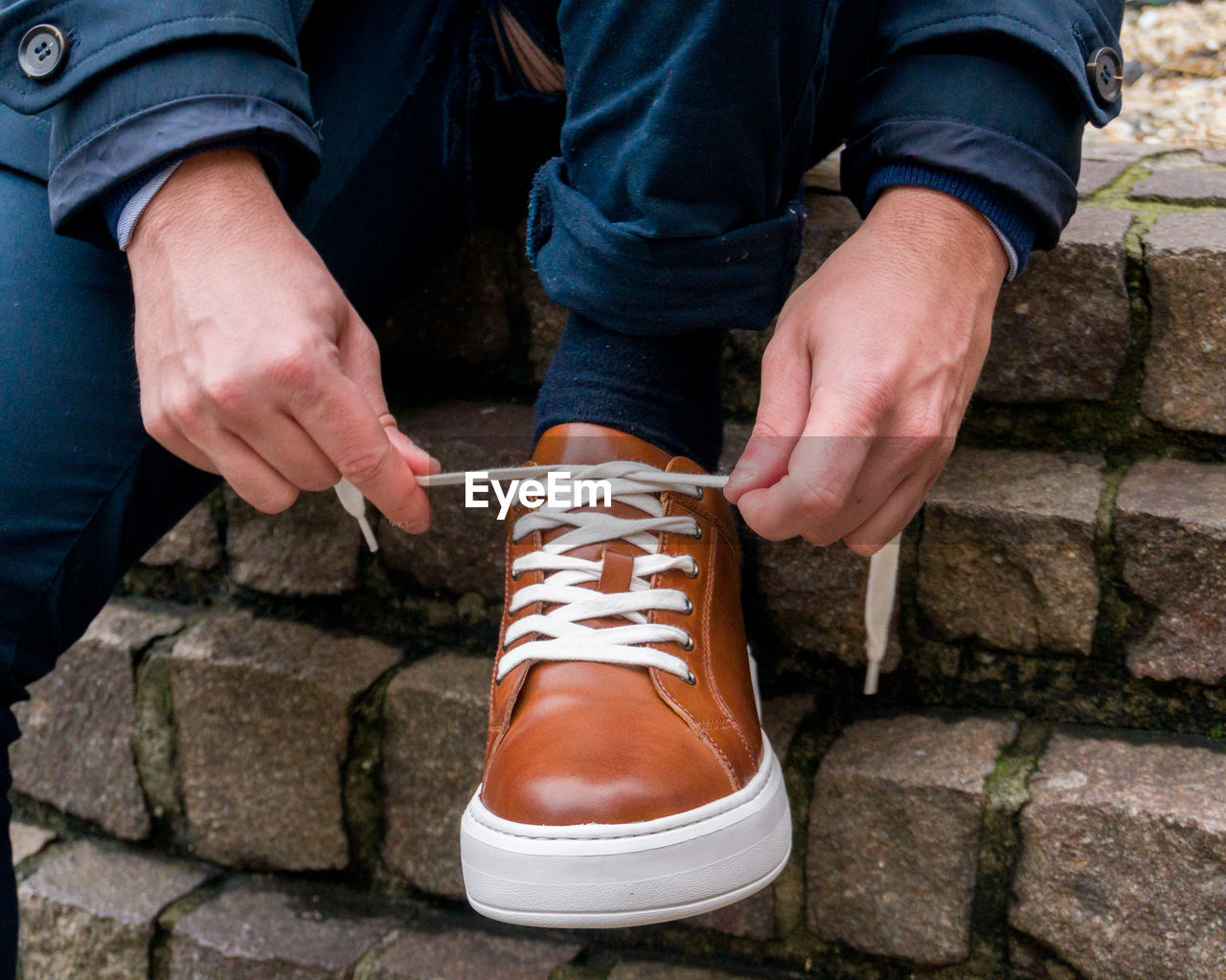 Low section of man lacing in shoes on concrete footpath