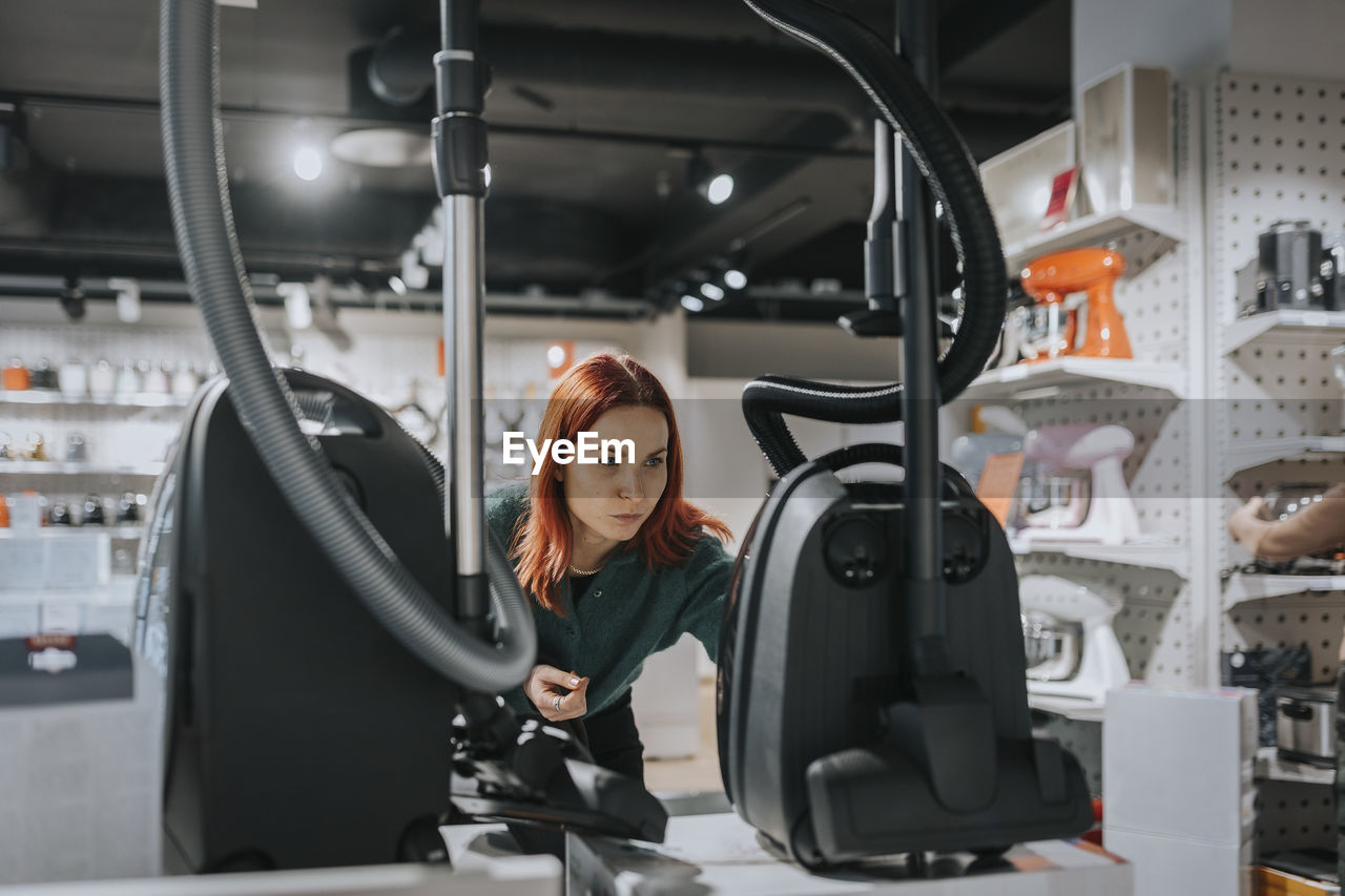 Female customer examining vacuum cleaner while shopping in modern electronics store