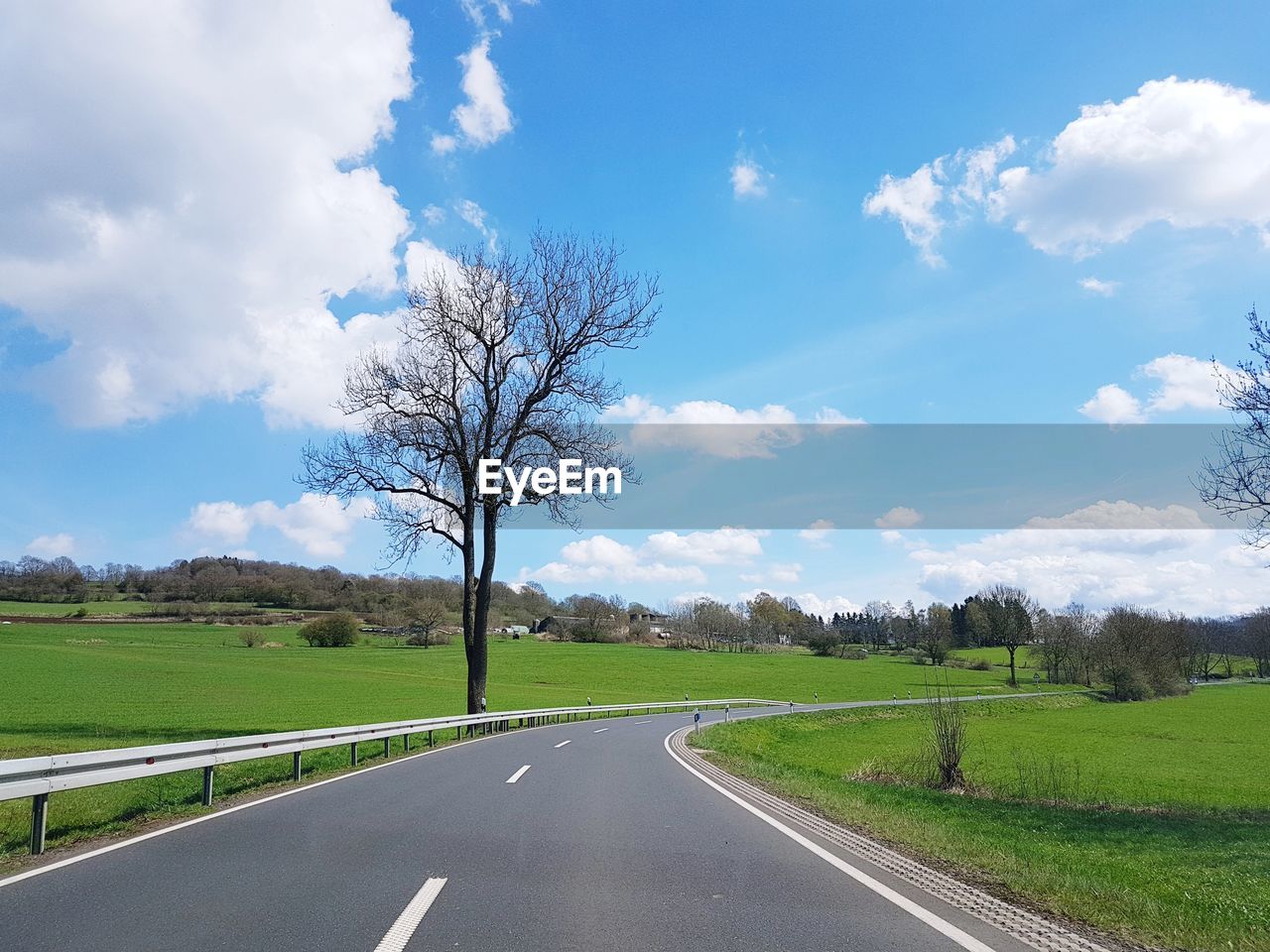 Road by trees on field against sky