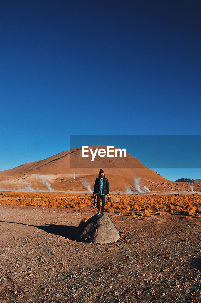 Full length of man standing on desert against clear blue sky