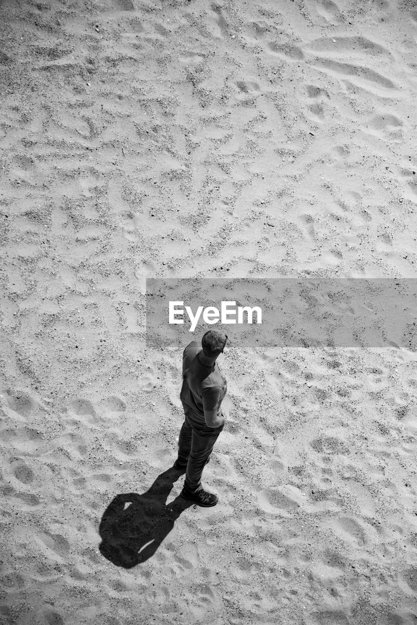 HIGH ANGLE VIEW OF WOMAN STANDING ON SAND