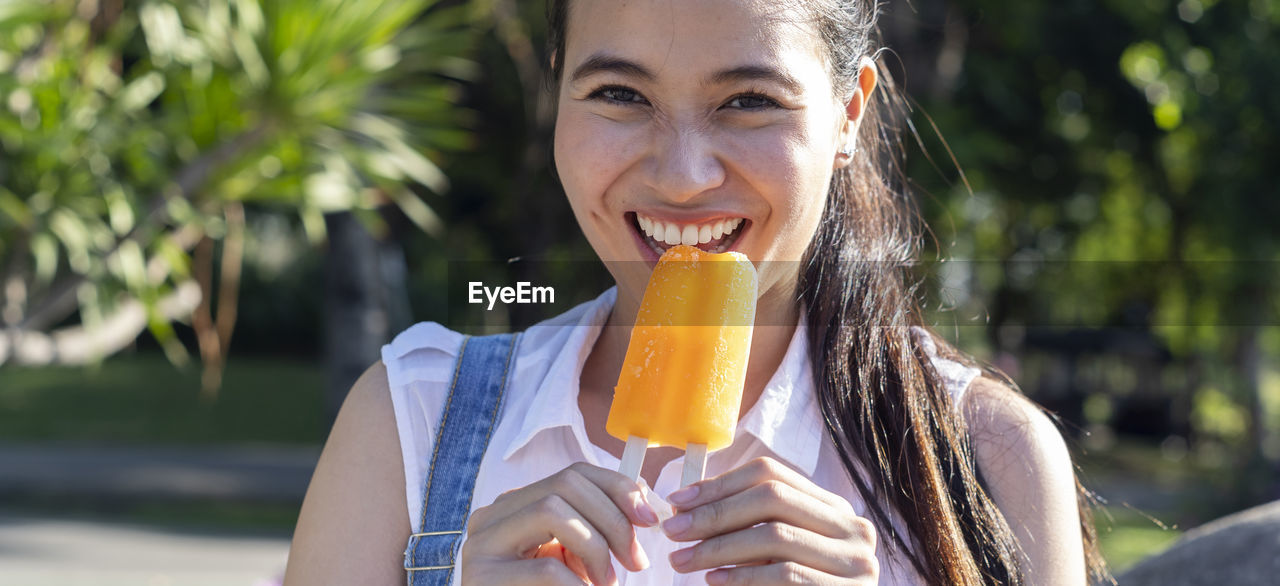 Close-up portrait of cheerful young woman eating popsicle