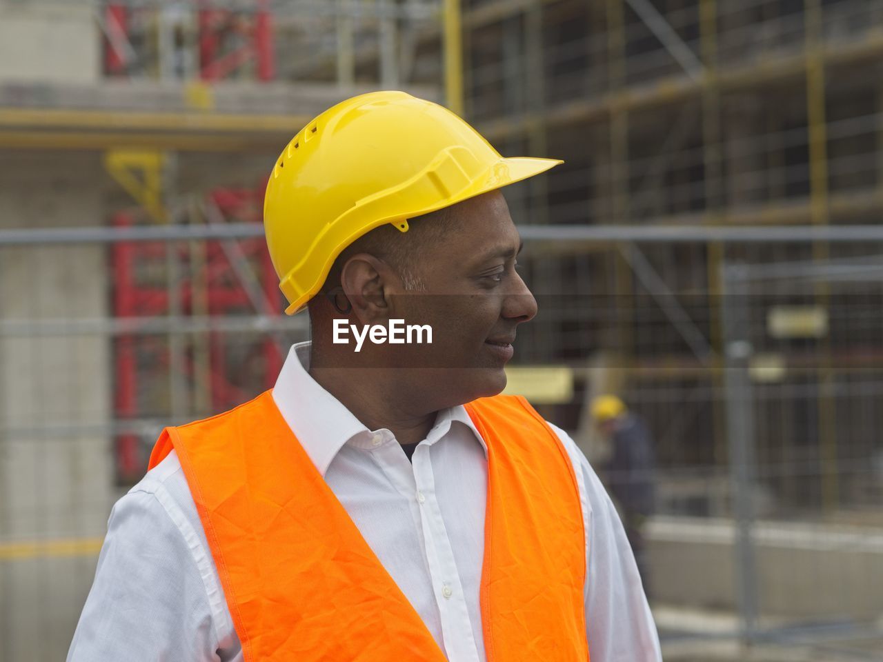 Side view of a smiling civil engineer or factory worker wearing a safety helmet and looking aside