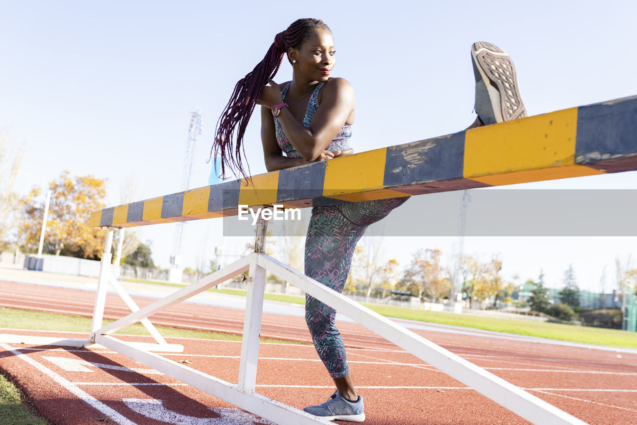 Sportswoman doing warm up exercise on balance beam against clear sky during sunny day