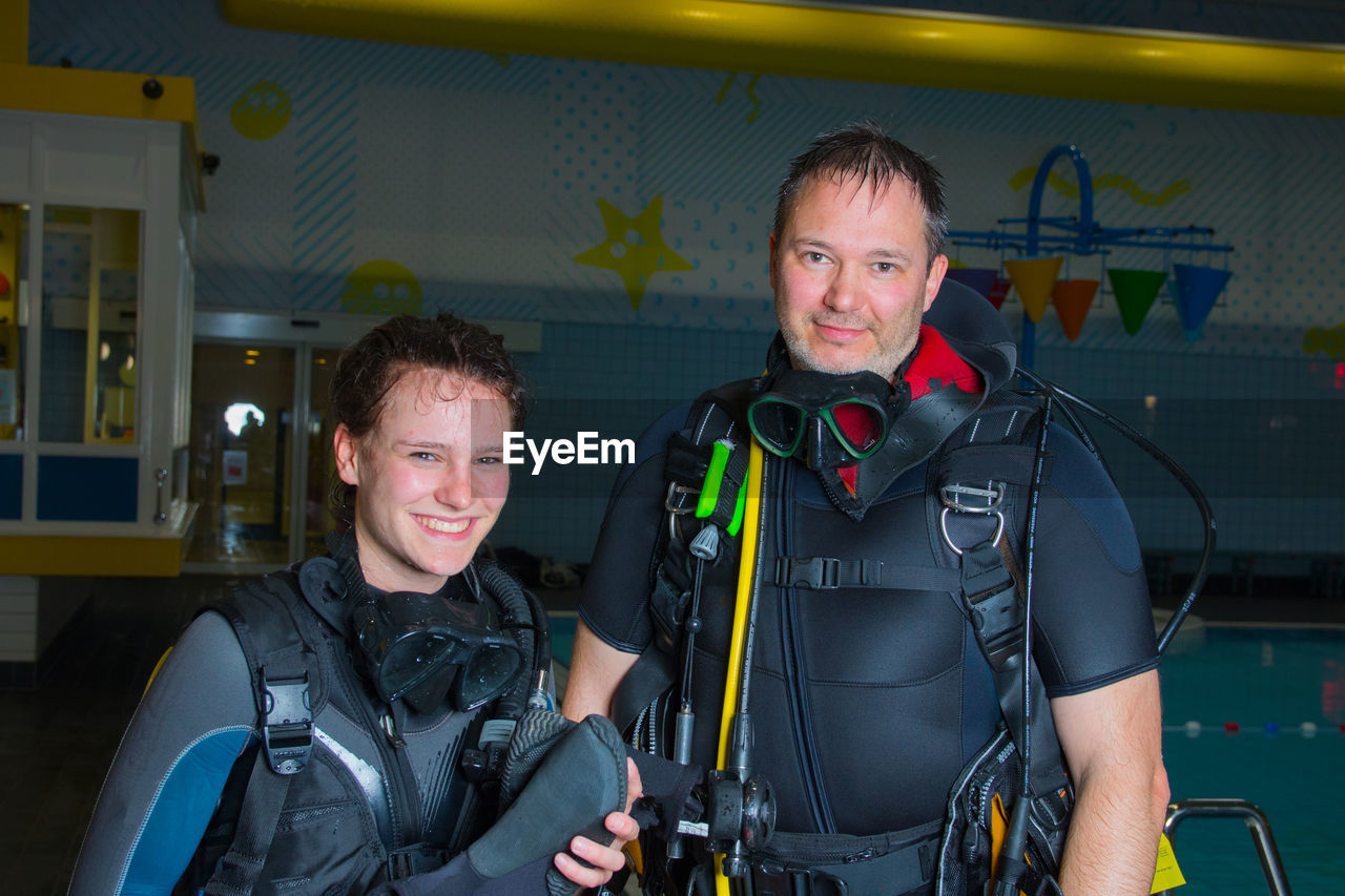 Portrait of smiling female scuba diver with instructor holding diving equipment