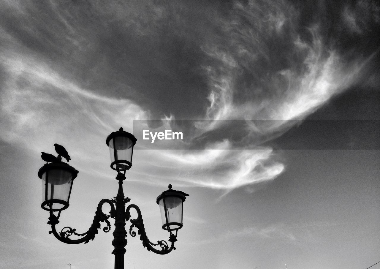 LOW ANGLE VIEW OF STREET LIGHTS AGAINST CLOUDY SKY