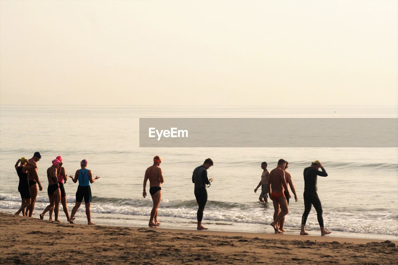 Swimmers walking at beach against clear sky