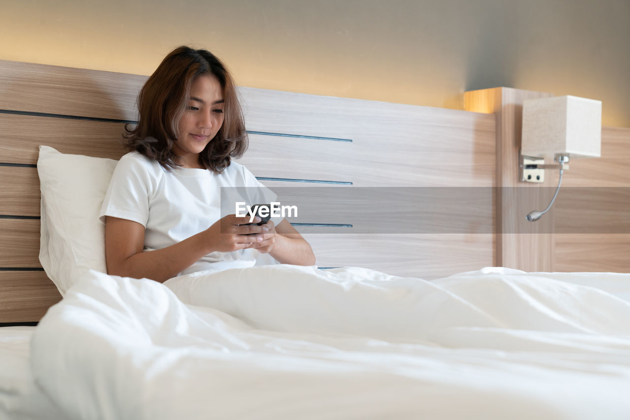 YOUNG WOMAN USING PHONE ON BED