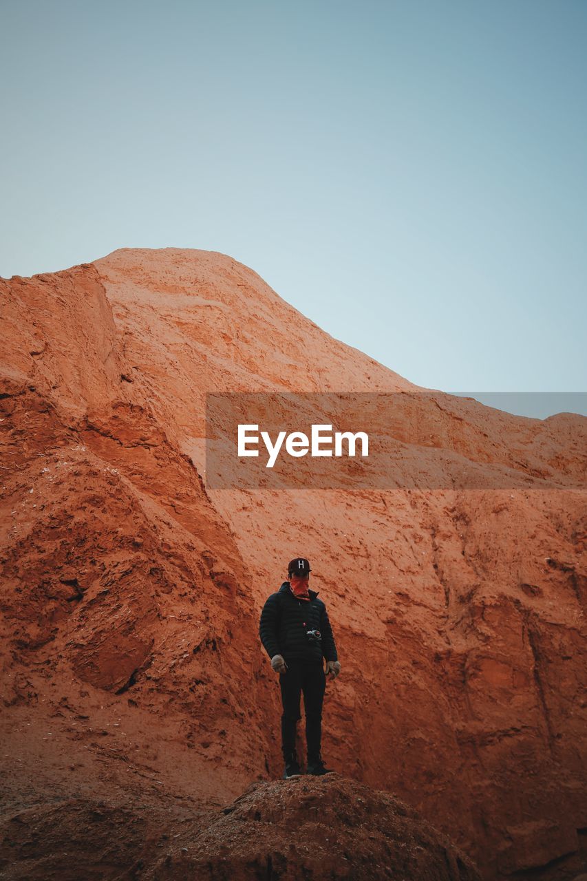 Young man standing on cliff against clear sky