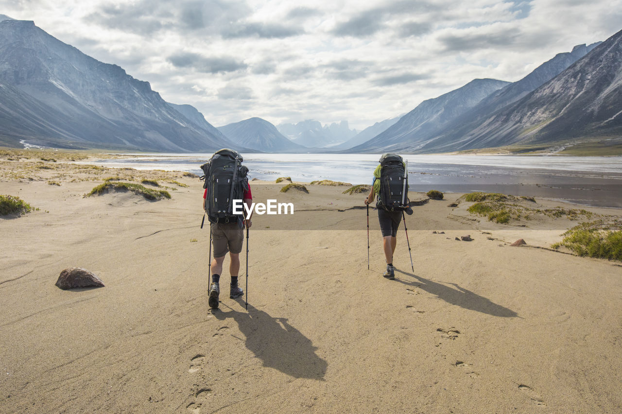 Rear view of two backpackers hiking, leaving footprints in the sand.