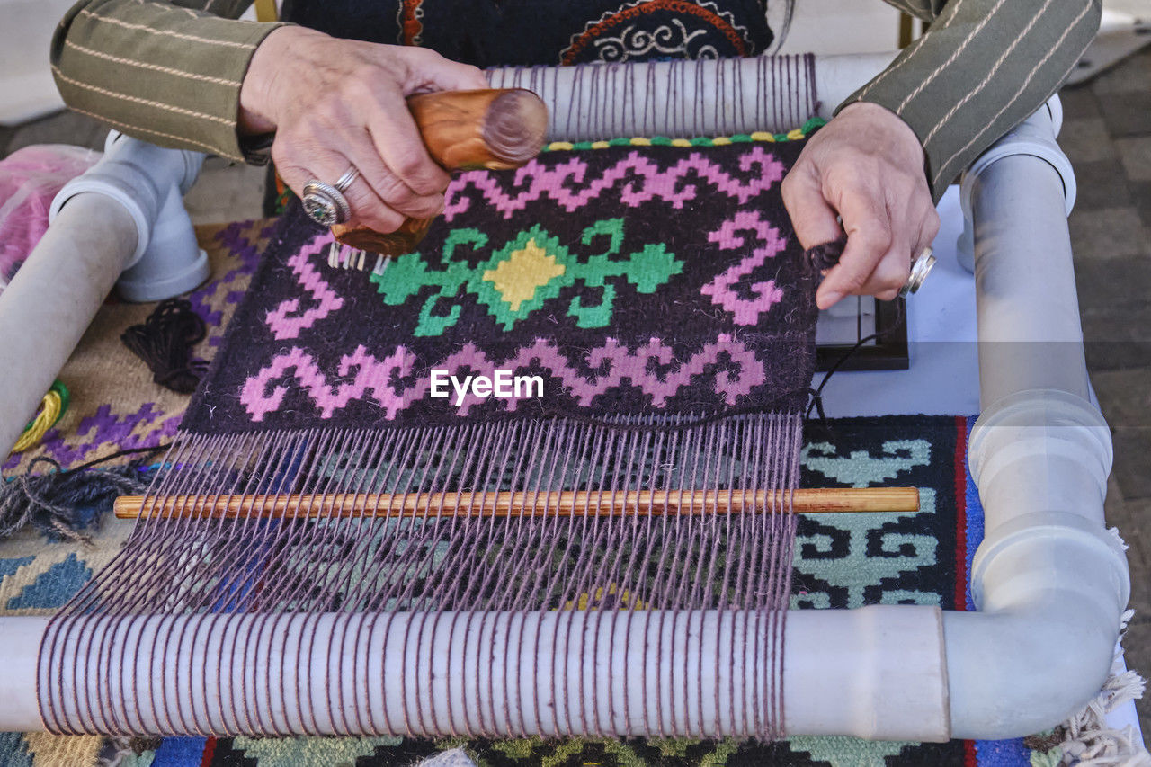 Hands of senior woman weaving a carpet with traditional asian pattern on table handloom