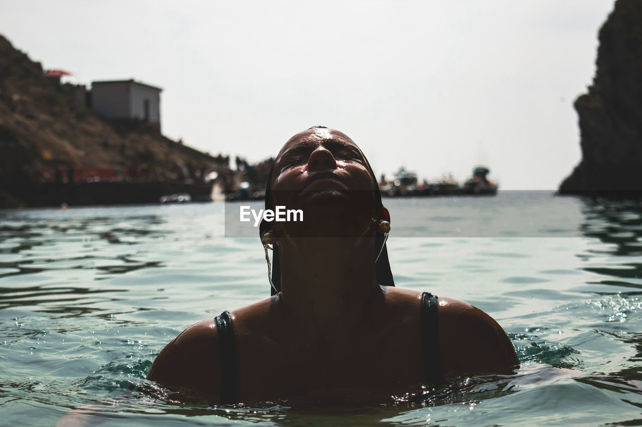 Woman swimming in lake against sky during sunny day