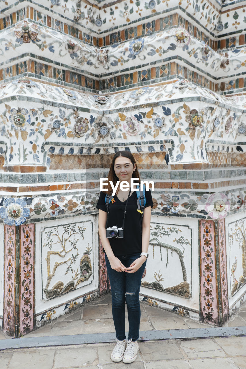 FULL LENGTH PORTRAIT OF WOMAN STANDING AGAINST BUILDING