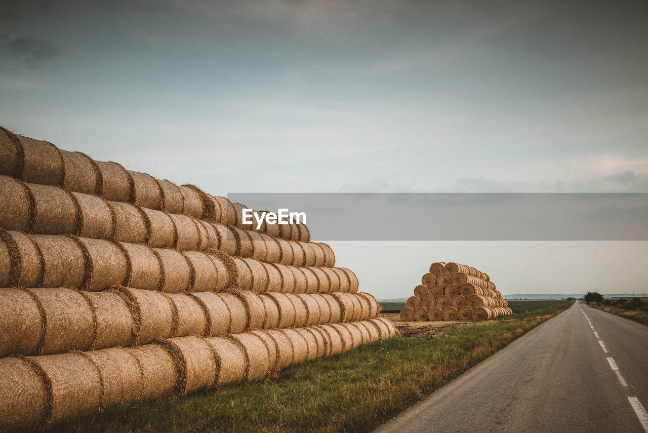 Stack of road by agricultural field against sky