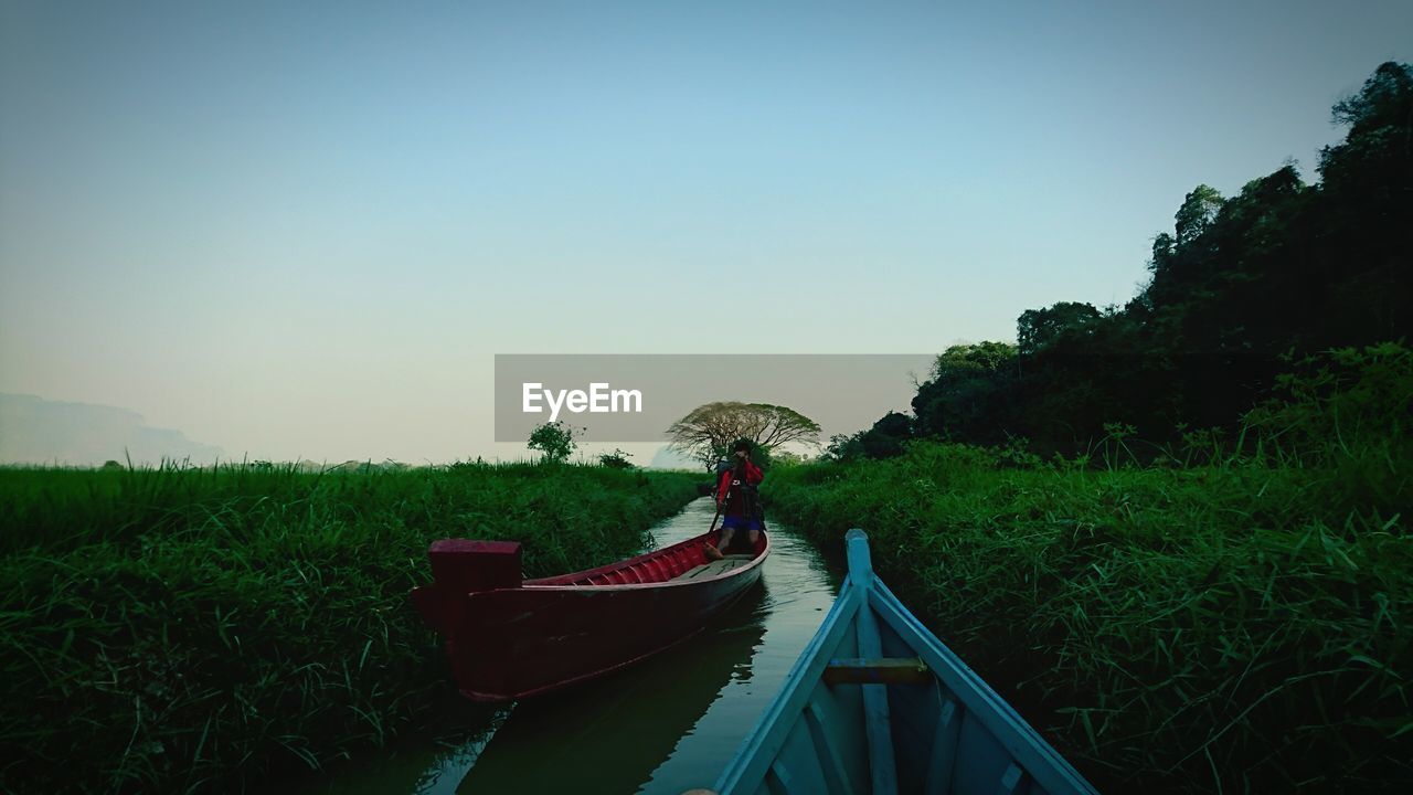 Person canoeing amidst field on canal against clear sky