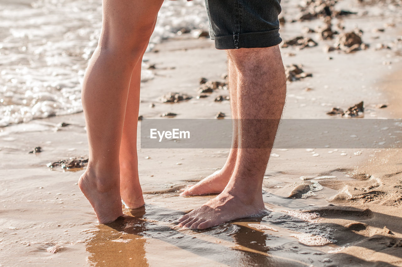 Low section of couple standing on shore at beach