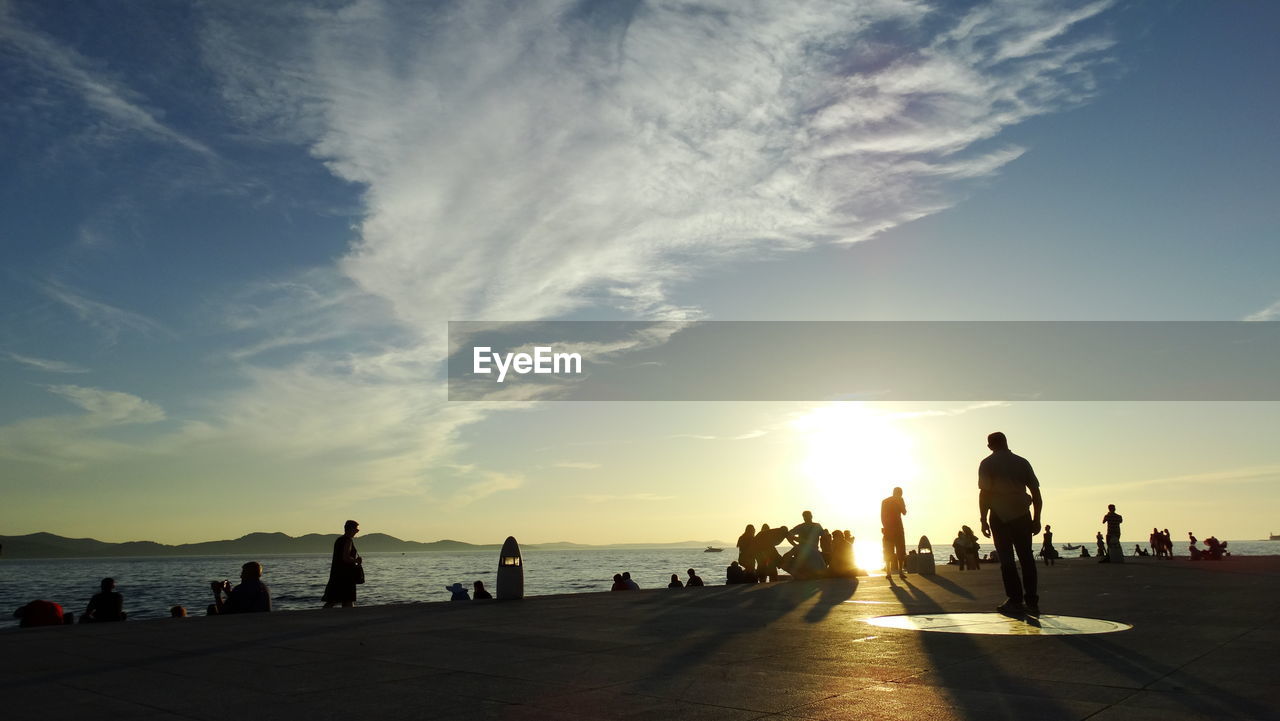 People at beach against sky during sunset